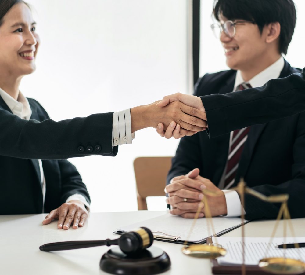 Female lawyer shaking hands with client after discussing deal of Female lawyer shaking hands with client after discussing deal of agreement together and signing contract on the table with brass scales and justice hammer in law firm.